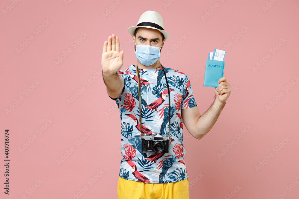 Dissatisfied traveler tourist man in mask to safe from coronavirus hold passport tickets showing stop gesture isolated on pink background. Passenger traveling on weekend. Air flight journey concept.