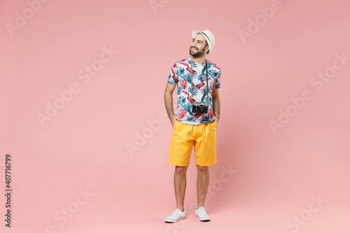 Full length funny young traveler tourist man in summer clothes hat with photo camera looking aside up isolated on pink background studio. Passenger traveling on weekends. Air flight journey concept.