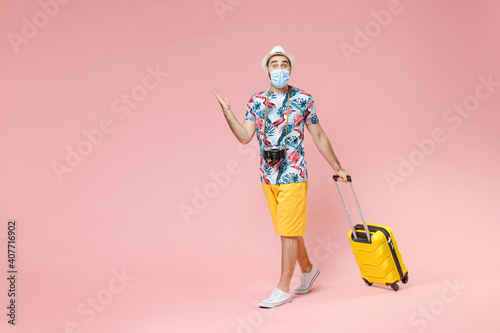 Full length shocked traveler tourist man in sterile face mask to safe from coronavirus covid-19 spreading hands isolated on pink background. Passenger travel on weekends. Air flight journey concept.