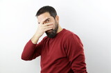Bearded man wearing casual clothes peeking in shock covering face and eyes with hand, looking through fingers with serious expression.