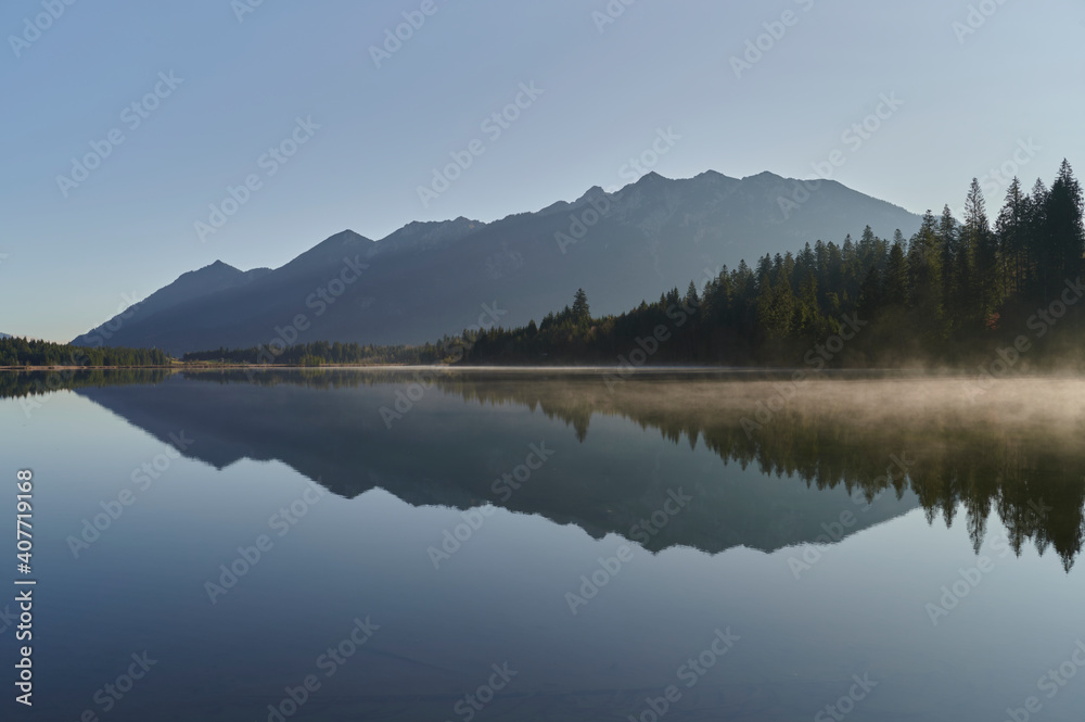 Spiegelung des Karwendelgebirges in einem See im Bayerischen Alpenvorland am frühen Morgen