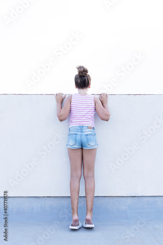 Young girl with her back against a wall facing the other way