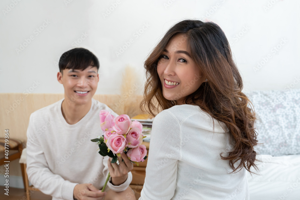 Selective focus of happy Asian young woman gets bouquet of pink flowers from her boyfriend at bedroom Selective focus of happy Asian young woman gets bouquet of pink flowers from her boyfriend at bedroom