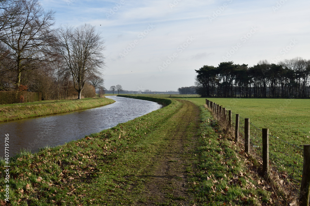 Beautiful Netherlands canal in the countryside with trees and footpath on the riverbank
