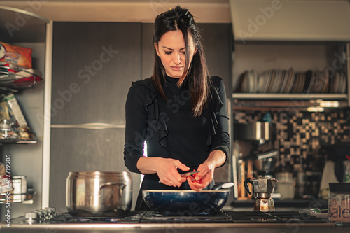 Housewife slicing tomatoes in the cooking pan. Young Italian woman making pasta sauce in the kitchen.