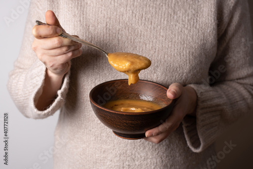 Female hands holding a spoon and a bowl of red lentil cream soup.