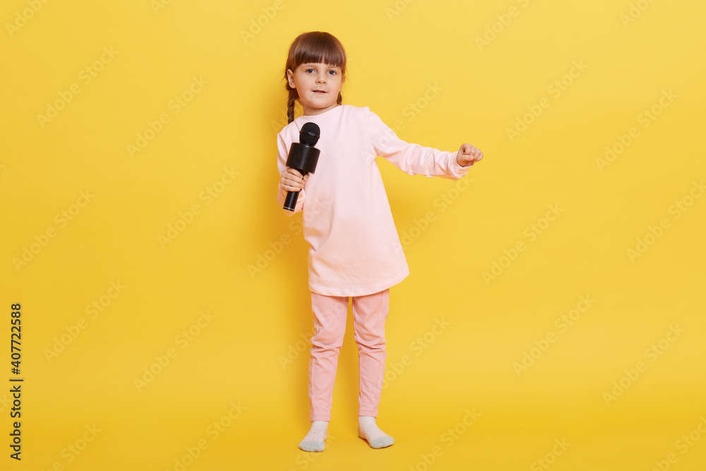 Little European girl singing with microphone, looks at camera, singing in karaoke, performing, making show, arranging concert, small vocalist performs. Little European girl singing with microphone, looks at camera, singing in karaoke, performing, making show, arranging concert, small vocalist performs.