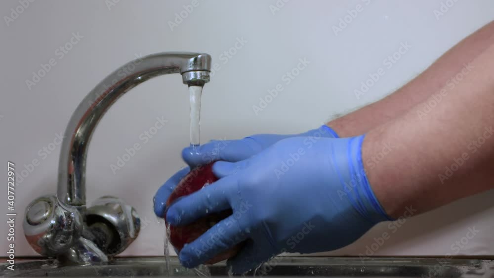 Male hands in gloves wash a red pomegranate and examine it. Rinsing fruit with water close-up under the tap. The blogger disinfects food. Fresh harvest, vegetarian food, home cooking. Male hands in gloves wash a red pomegranate and examine it. Rinsing fruit with water close-up under the tap. The blogger disinfects food. Fresh harvest, vegetarian food, home cooking.