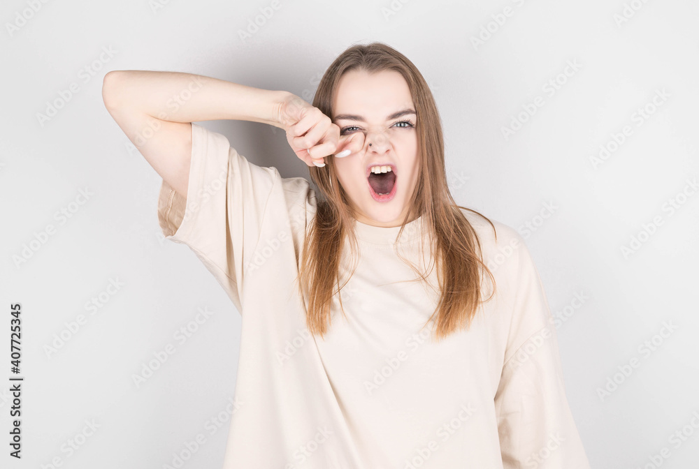 Young woman with disheveled hair yawns from fatigue against gray wall Young woman with disheveled hair yawns from fatigue against gray wall