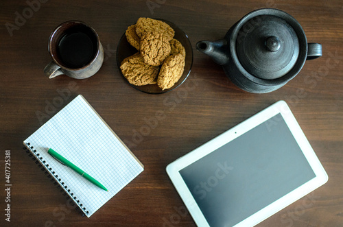 The table on which there is a mug of tea biscuits, a notebook, a pen.