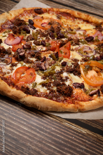 Top view of fresh baked pizza with meat and vegetables on a wooden table. Pizza delivery. Take away. 