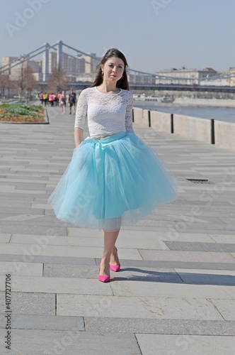 A girl in a blue fluffy skirt and pink shoes walks along a city street