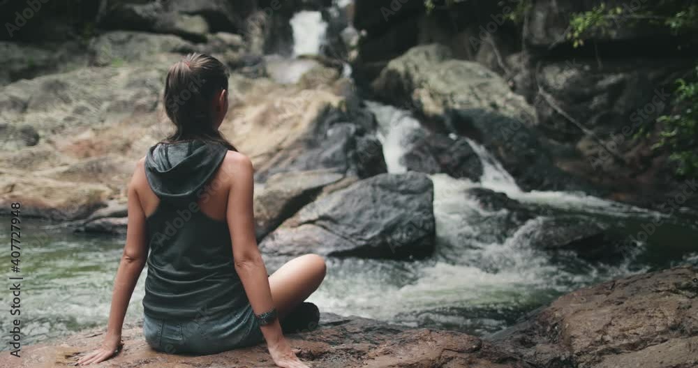 Thailand's river waterfall: woman rest on stones. Calm water flow on stream rock bottom. Girl relaxing back view: National Park Than Sadet, Koh Phangan Island. Cinematic footage shot in 4K, UHD Thailand's river waterfall: woman rest on stones. Calm water flow on stream rock bottom. Girl relaxing back view: National Park Than Sadet, Koh Phangan Island. Cinematic footage shot in 4K, UHD