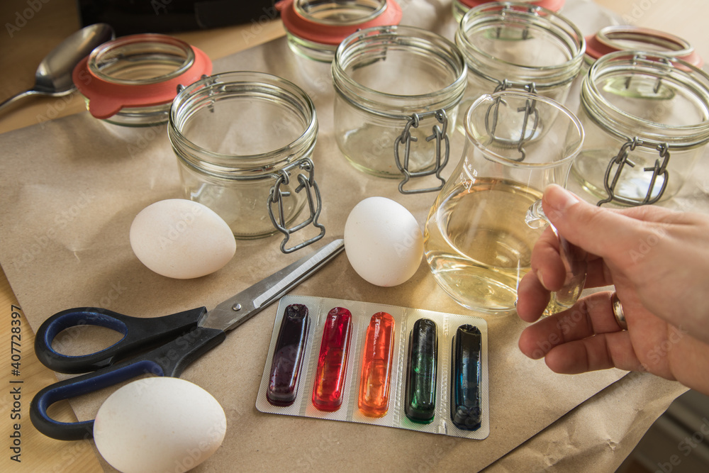 Frau mit Essig, Wasser und bunten Ostereier Kaltfarben in Rot, Orange, Gelb, Blau, Grün in Verpackung auf Papier Unterlage mit Gläser, gekochte Eier und Schere zum Färben zu Ostern Frau mit Essig, Wasser und bunten Ostereier Kaltfarben in Rot, Orange, Gelb, Blau, Grün in Verpackung auf Papier Unterlage mit Gläser, gekochte Eier und Schere zum Färben zu Ostern