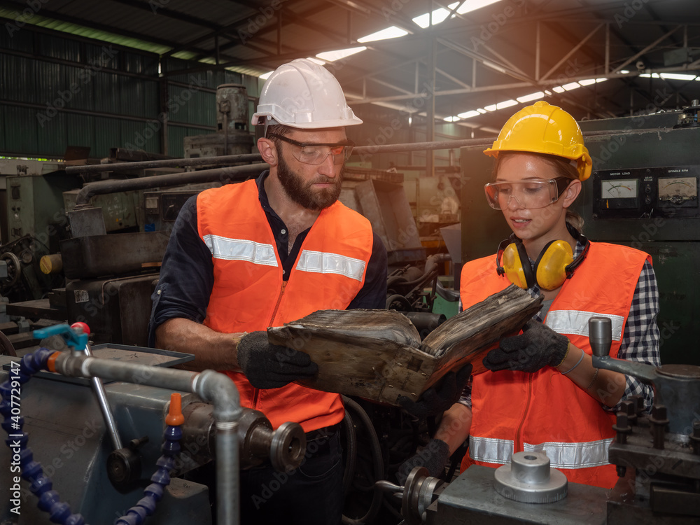 Confident young female mechanical engineer in a protective uniform, helmet while listening to colleague explanation workflow the CNC Machinery while working at the plant. Confident young female mechanical engineer in a protective uniform, helmet while listening to colleague explanation workflow the CNC Machinery while working at the plant.