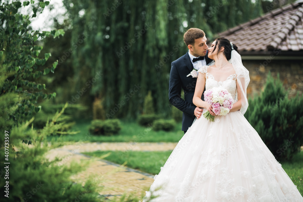 Beautiful bride and groom embracing and kissing on their wedding day outdoors Beautiful bride and groom embracing and kissing on their wedding day outdoors