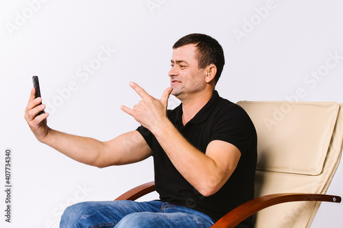 A man sitting in a leather armchair communicates non-verbally via video communication, showing I Love You to his soulmate. White background. photo