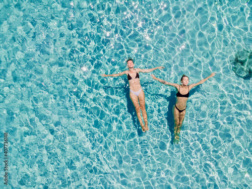 Couple of woman floating in clear blue sea. Aerial view