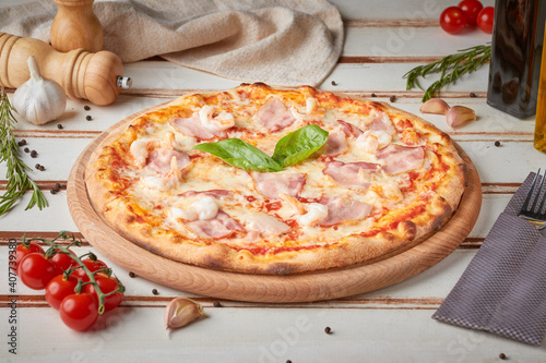 Pizza with slices, sauce and herbs, wooden white background