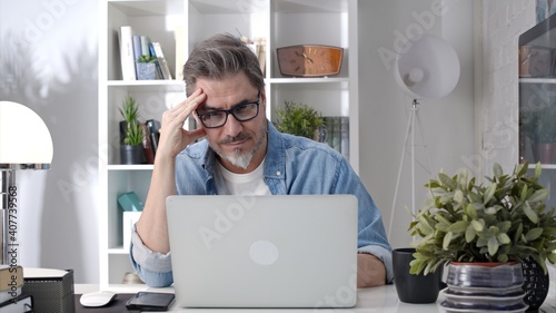 Older man working online with laptop computer at home sitting at desk. Home office, browsing internet, study room, entrepreneur.