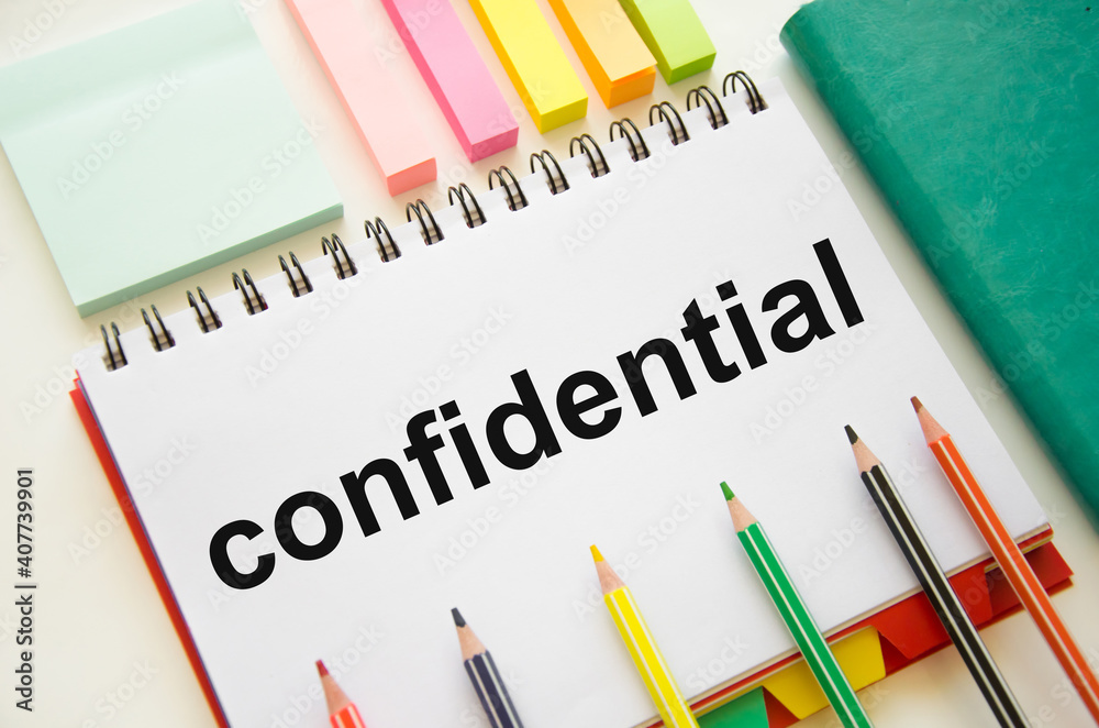 the word confidential written on a white notepad which lies on a white background near a green notepad and stickers