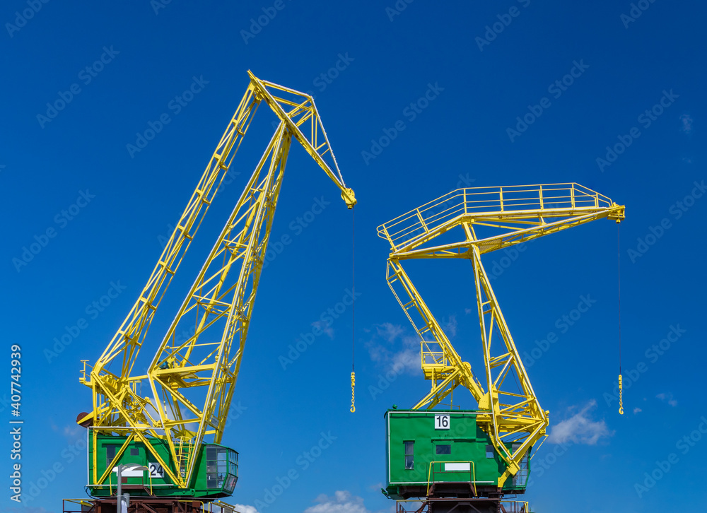 two colorful industrial cranes on a blue sky background two colorful industrial cranes on a blue sky background