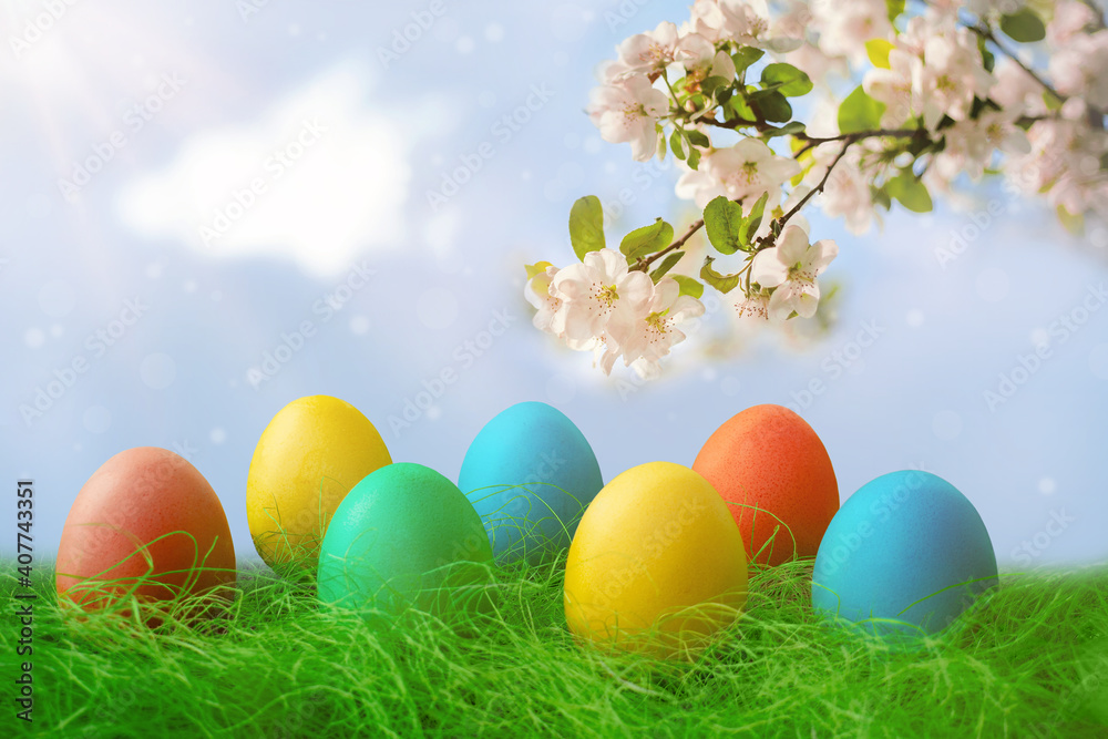 Happy Easter. A row of decorative Easter eggs on the green grass. On the background of the sky and apple tree flowers Happy Easter. A row of decorative Easter eggs on the green grass. On the background of the sky and apple tree flowers
