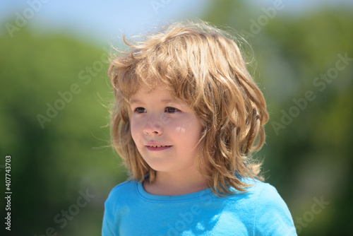 Closeup attractive kids face. Child emotions concept. Portrait of young smiling kid outdoor. Blur background.