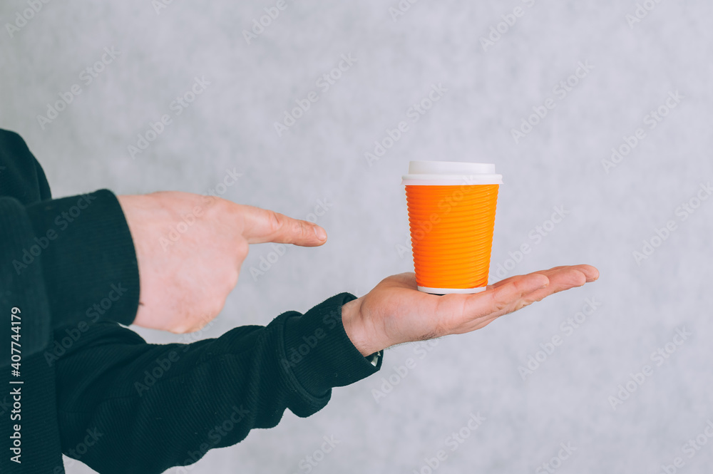 A man holds a mock-up of a paper cup for coffee and tea on a light background. A man holds a mock-up of a paper cup for coffee and tea on a light background.