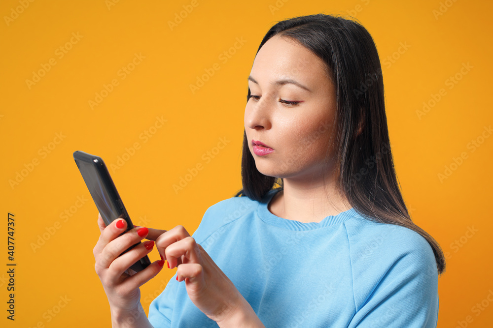 Young woman using smartphone and smiling on a yellow background. Young woman using smartphone and smiling on a yellow background.
