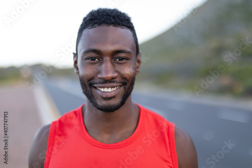 Portrait of fit african american man standing on a coastal road looking at camera smiling
