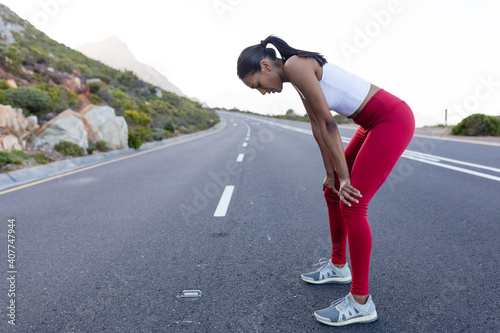 Fit african american woman in sportswear standing and resting on a coastal road