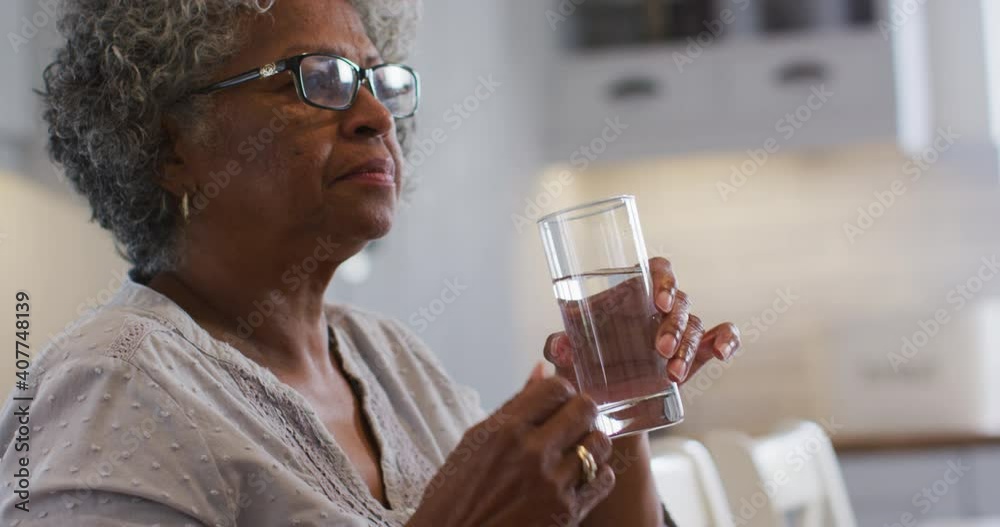 Senior african american woman taking medication and drinking water while sitting at home