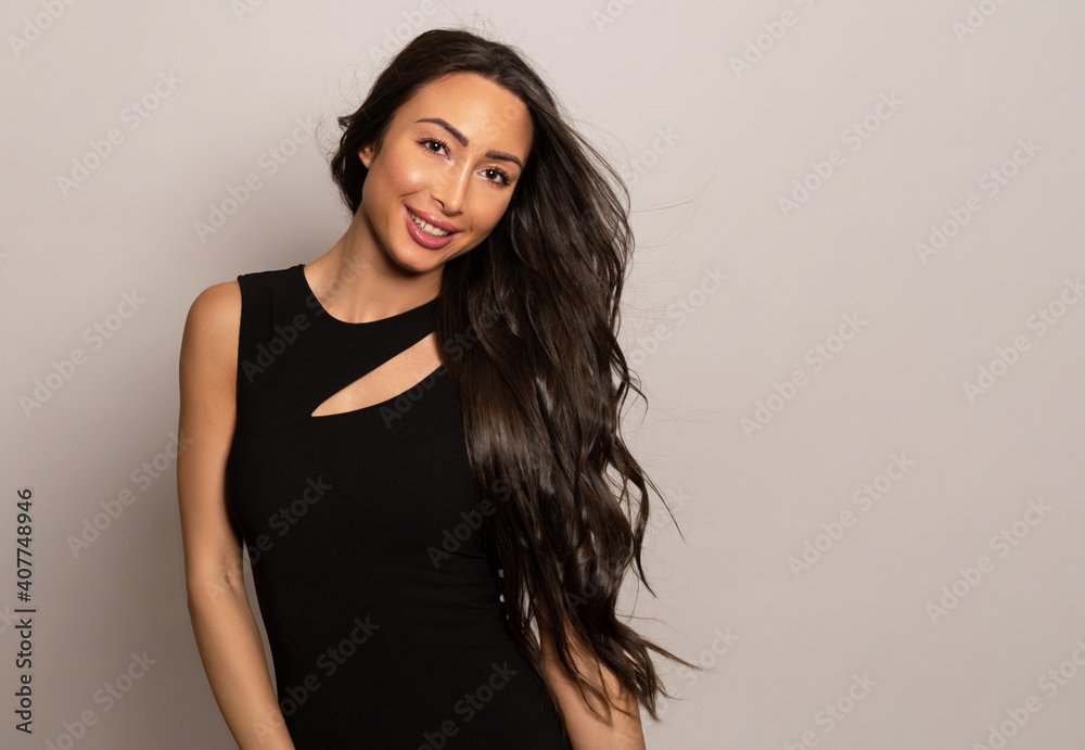 Beautiful young woman with long shiny black hair and natural make-up posing in dress on grey background Beautiful young woman with long shiny black hair and natural make-up posing in dress on grey background