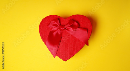 Close up of red gift box in form of heart with bow on yellow background. Concept of holidays  presents and good mood.