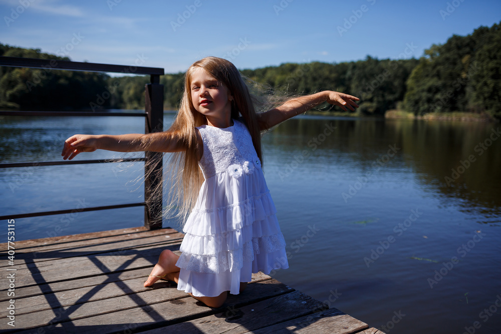 Portrait of a little girl outdoors in the summer by the lake. Little girl in summer dress by the river.