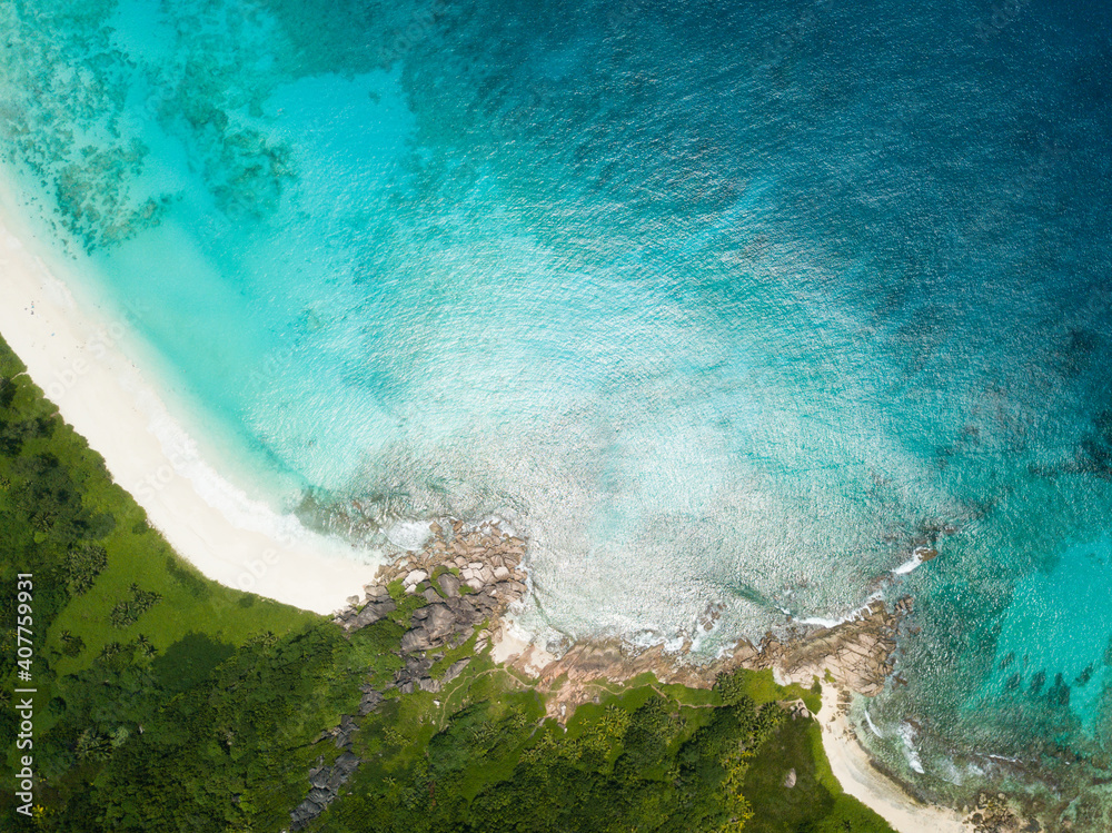 Beautiful tropical island beach with blue sea, green vegetation and white sand with typical Seychelles granite rocks from high above, birds eye view drone image.