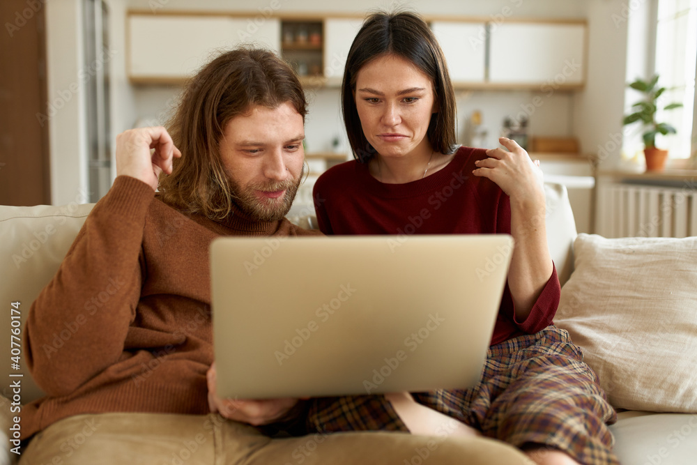 People, family, domestic life and electronic devices. Handsome guy with beard having rest indoors sitting on couch with his dark haired wife enjoying favorite film together on portable computer People, family, domestic life and electronic devices. Handsome guy with beard having rest indoors sitting on couch with his dark haired wife enjoying favorite film together on portable computer