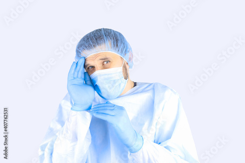 A man in a medical gown, mask and gloves raised his hand to his head in a gesture of embarrassment. © Roman