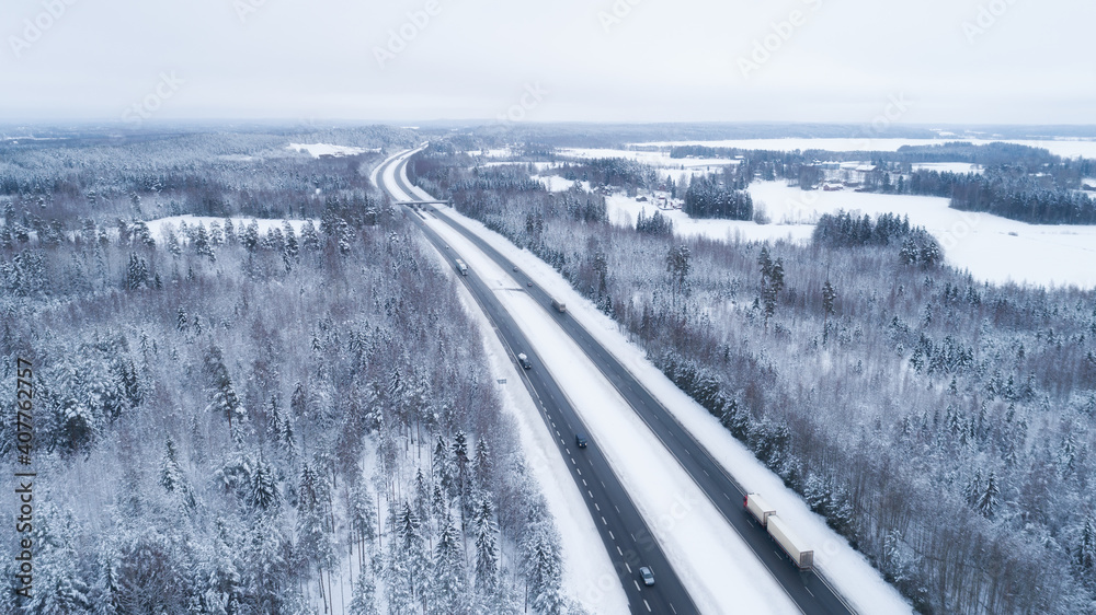 Aerial view of  winter asphalt highway or motorway road in countryside with cars and cargo logistic trucks in winter time