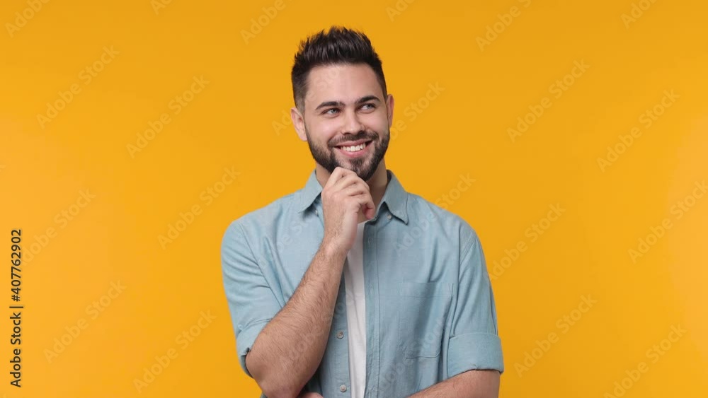 Smiling pensive bearded young man 20s in casual blue shirt white t-shirt isolated on yellow background in studio. People sincere emotions lifestyle concept. Looking aside up put hand prop up on chin Smiling pensive bearded young man 20s in casual blue shirt white t-shirt isolated on yellow background in studio. People sincere emotions lifestyle concept. Looking aside up put hand prop up on chin