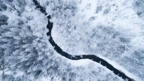 Aerial view of river thorugh snow covered forest in calm scene. Drone view photo from the drone on a cloudy day. Aerial top view beautiful snowy landscape. 