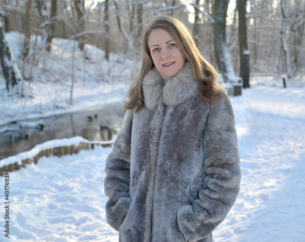 Young woman in a fur coat stands on the bank of a stream in a winter park Young woman in a fur coat stands on the bank of a stream in a winter park