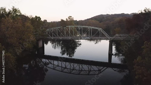 Slow push to an old iron bridge across calm water during a full sunrise.