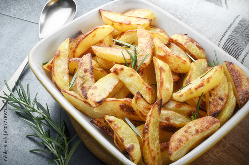 Roasted potatoes with rosemary in a baking dish on gray background.