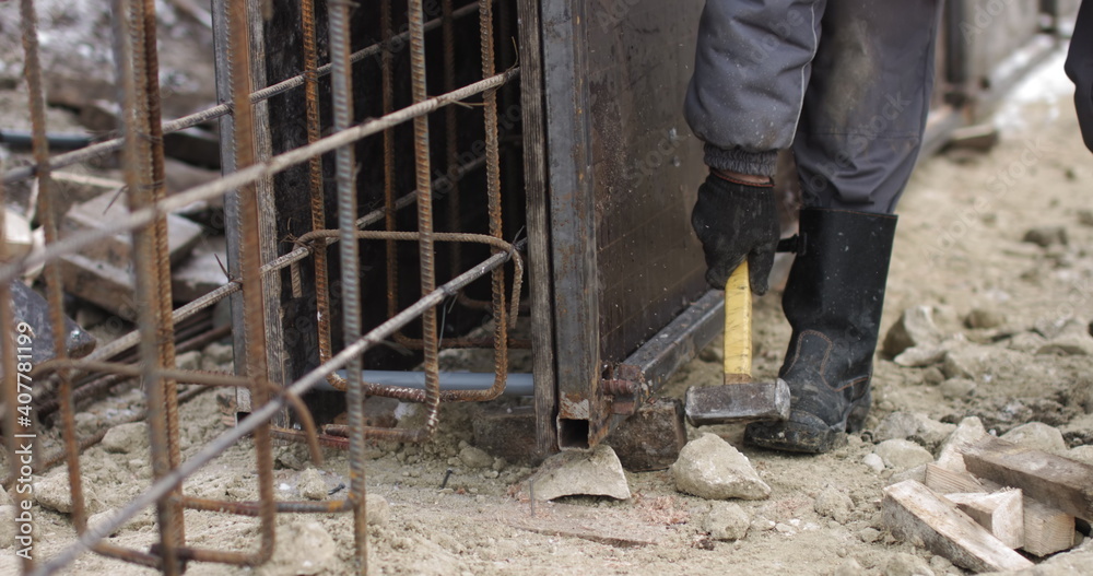 Engineers work with metal constructions while building a house. The worker fixes the form for pouring concrete, aligns metal boards. Filling the foundation of the building