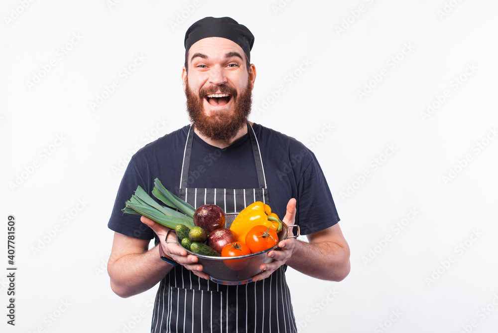 Photo of amazed young chef man in uniform holding some fresh vegetables. Photo of amazed young chef man in uniform holding some fresh vegetables.
