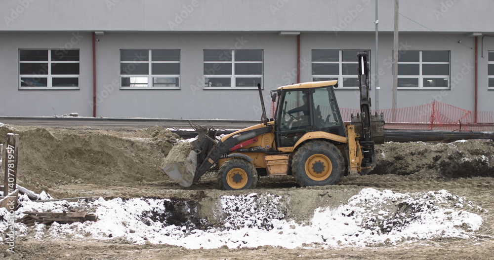 The bulldozer works on a construction site with sand, side view. New Big Tractor, a bulldozer on wheels on a sandy road on a construction site levels the site for the construction of real estate