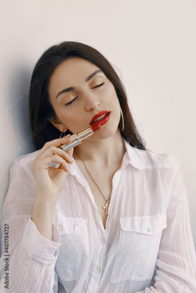 A very beautiful brunette girl with red lips is holding red lipstick in her hands. A very beautiful brunette girl with red lips is holding red lipstick in her hands.