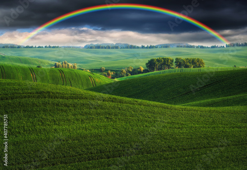  Scenic view of rainbow over green field. dramatic gray sky over a picturesque hilly field © sergnester